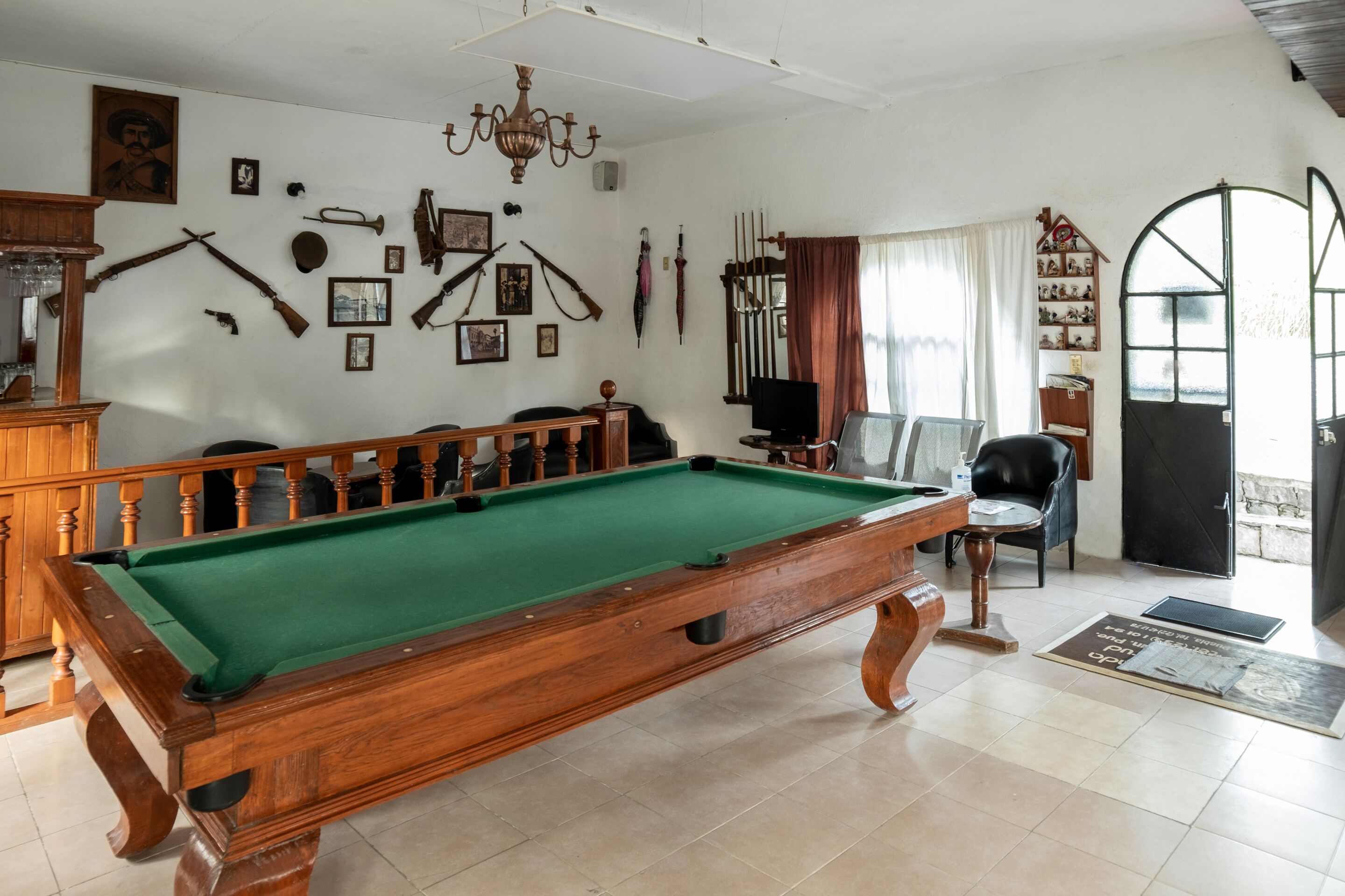A billiards room with a pool table, wooden furniture, and various wall-mounted items.