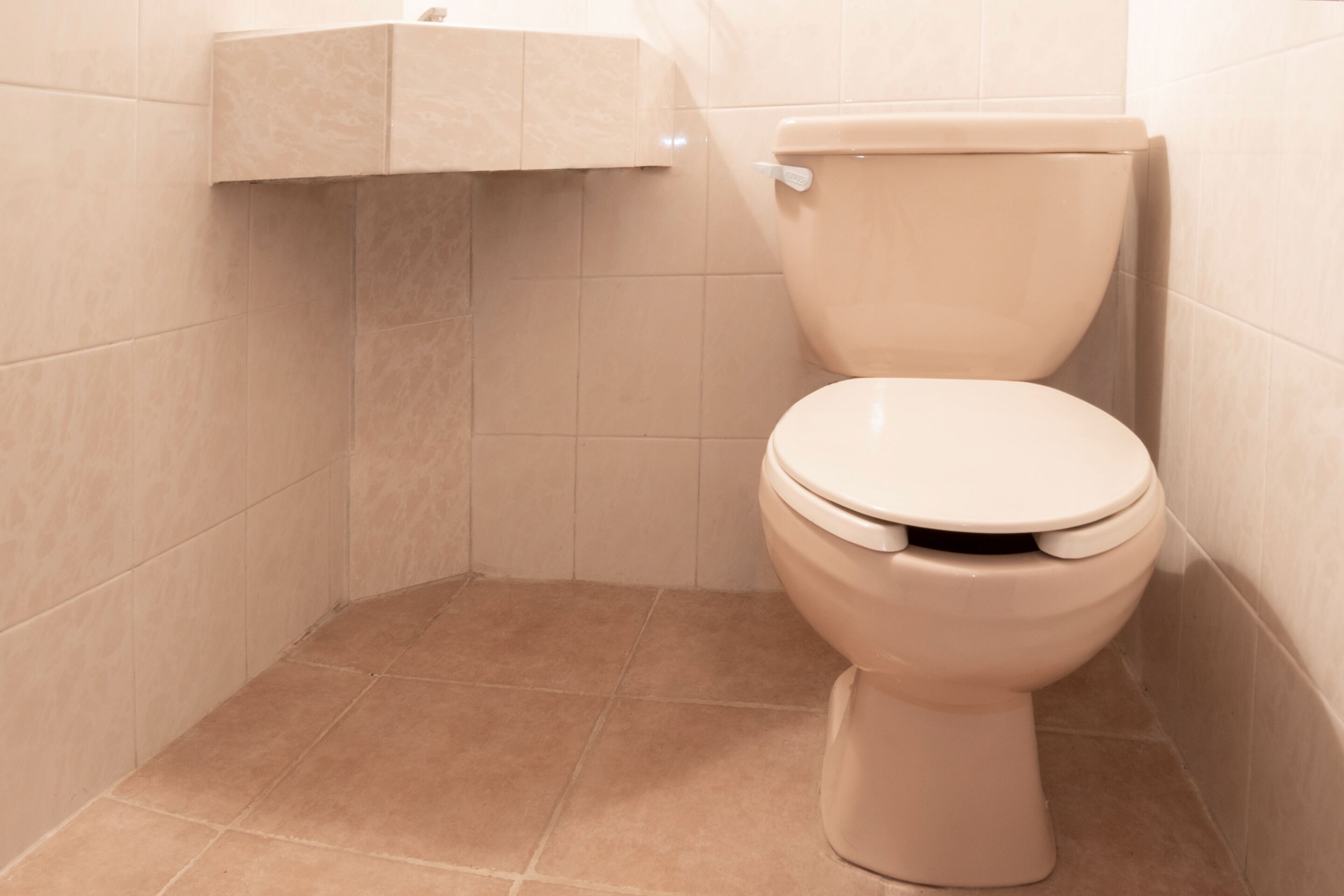 A toilet in a corner with beige tiles on the walls and floor.