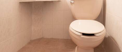 A toilet in a corner with beige tiles on the walls and floor.