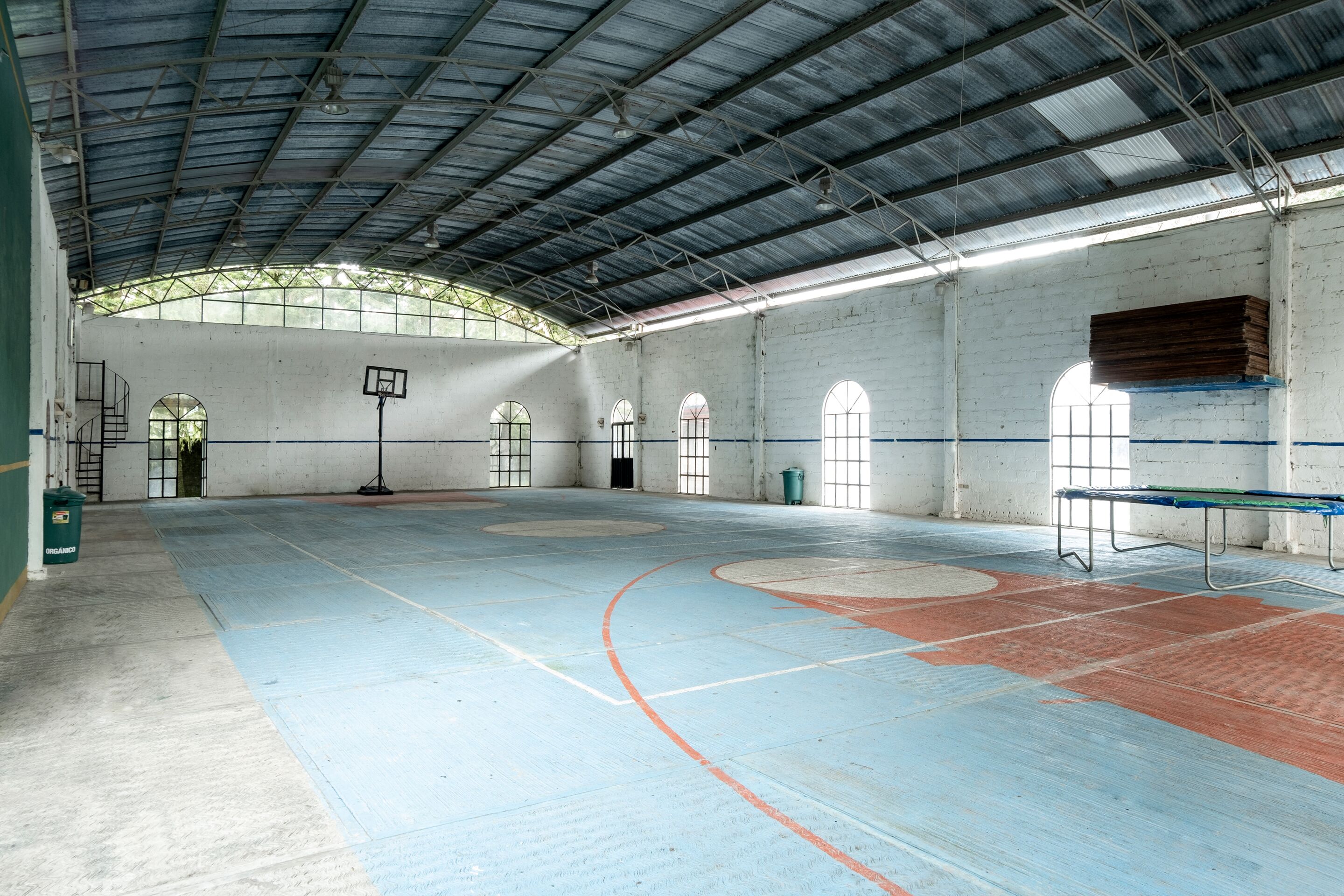 An indoor basketball court with a high ceiling, skylights, and a basketball hoop.