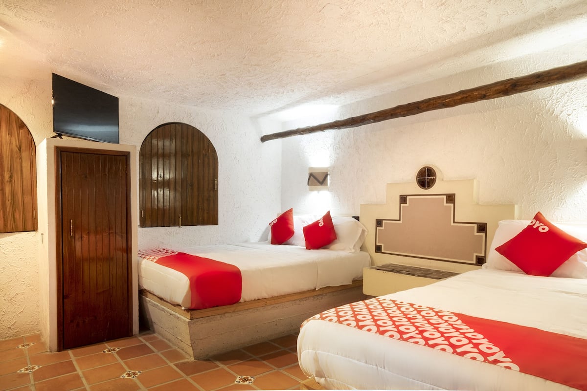 Una habitación con dos camas, una puerta de madera, un televisor y piso de baldosas.