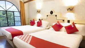 Een hotelkamer met twee bedden, elk voorzien van rode en witte beddengoed, een groot raam met uitzicht op bomen, en een houten vloer.