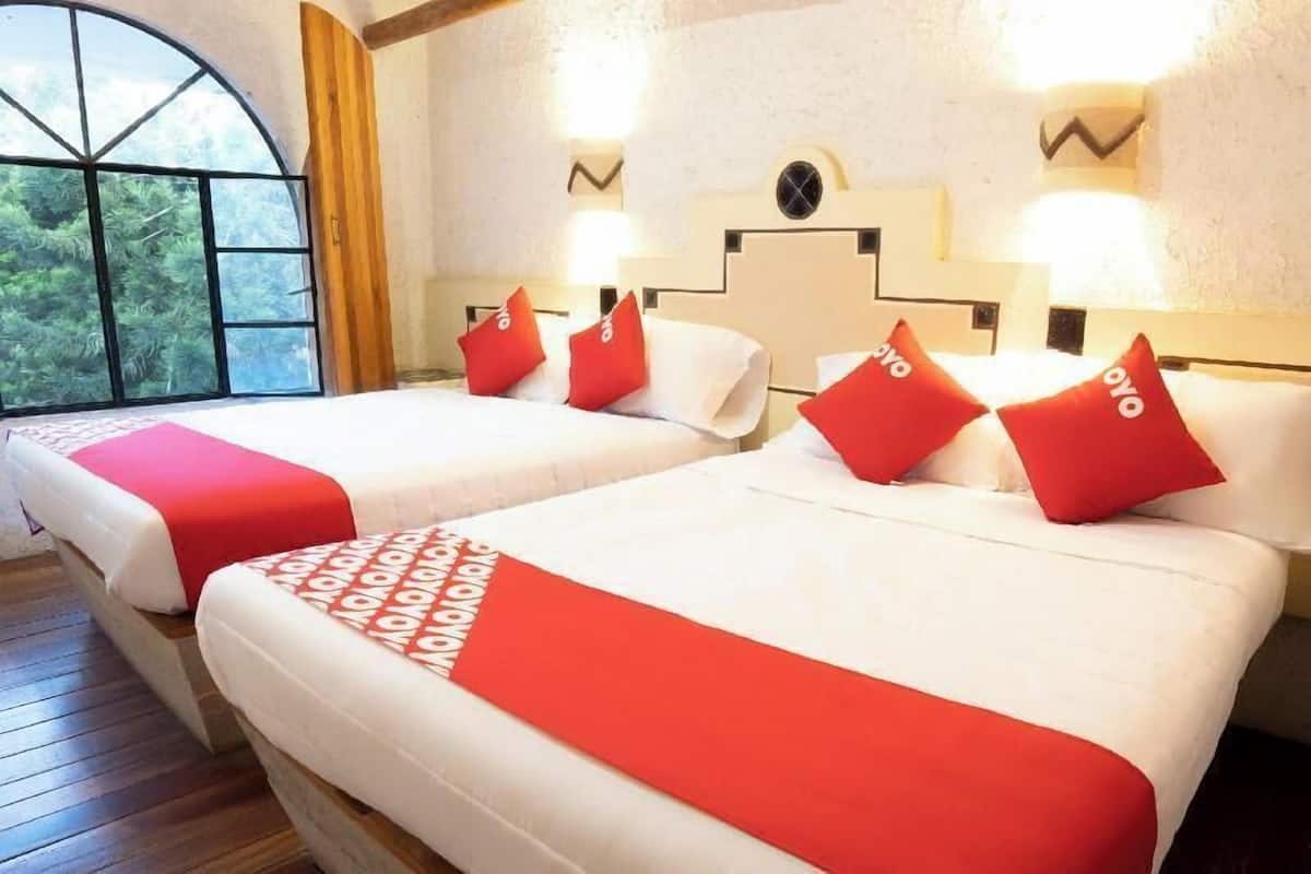 Habitación de hotel con dos camas, cada una con ropa de cama roja y blanca, y un ventanal con vistas a zonas verdes.