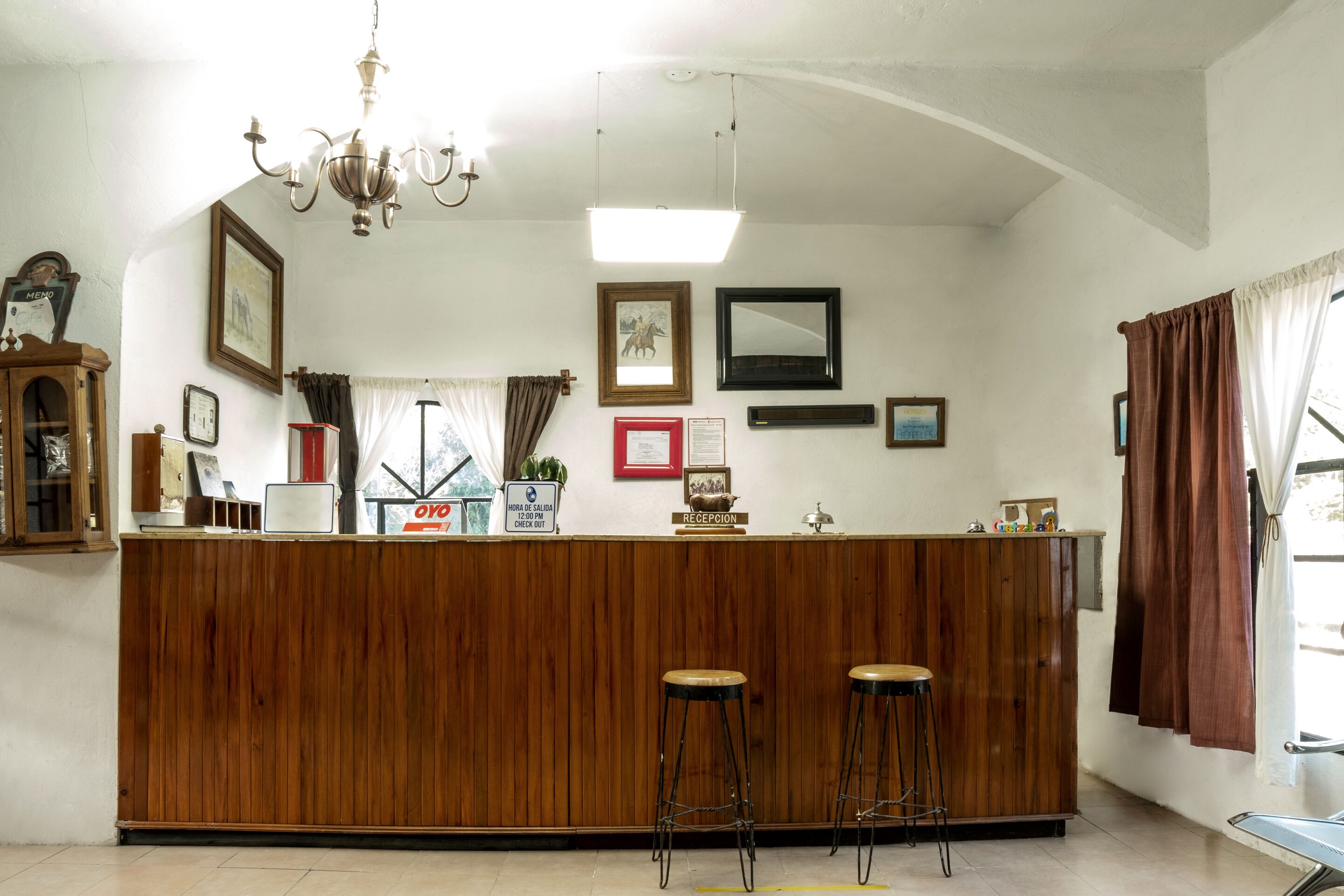 Una zona de recepción con mostrador de madera, dos taburetes tipo bar, una araña y cuadros en las paredes.