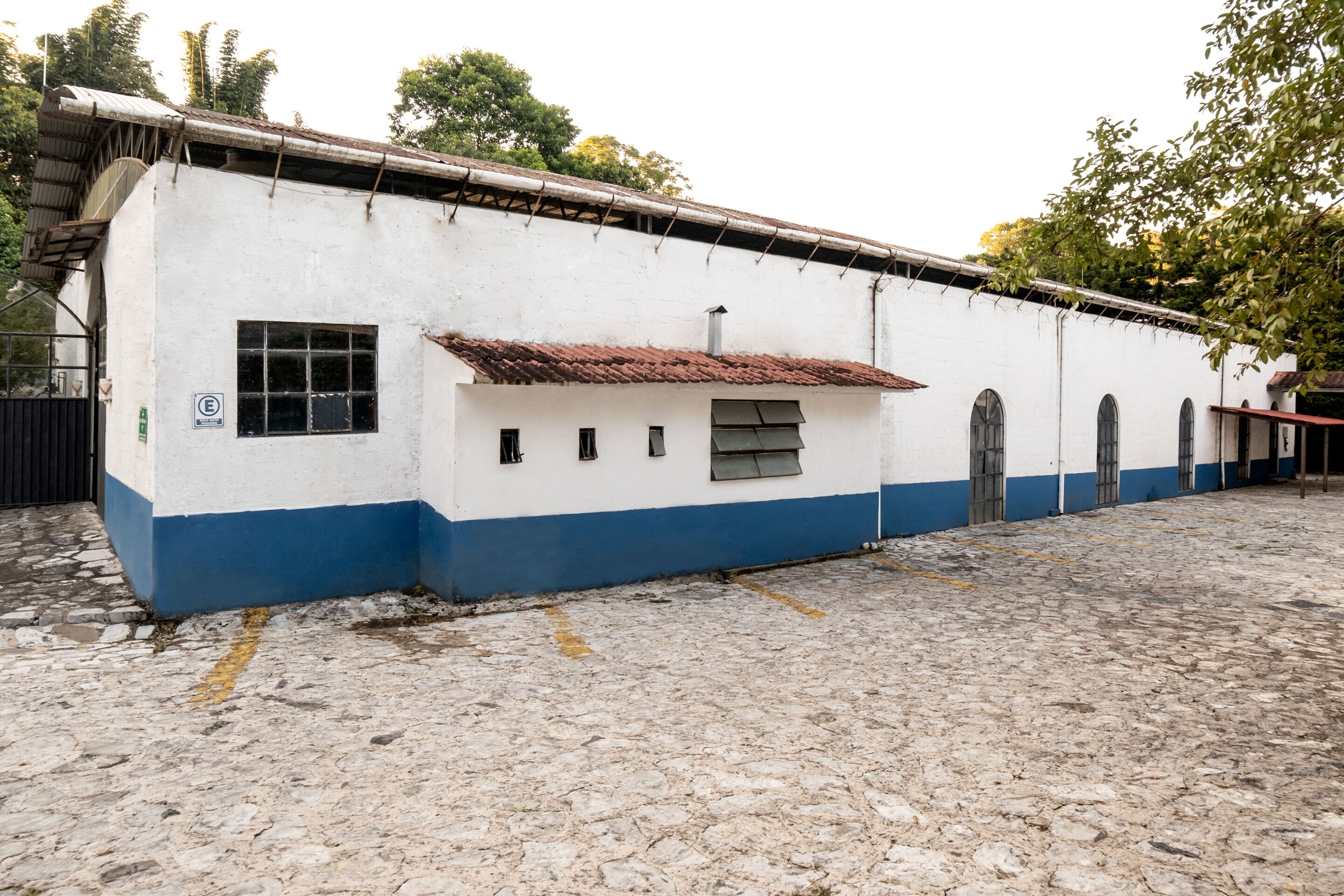 A building with a white and blue exterior, a tiled roof, and a cobblestone ground.