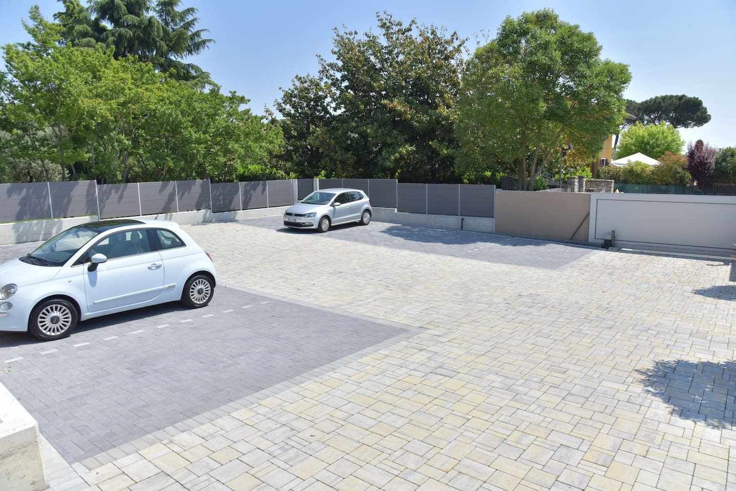 A paved parking area with two cars, surrounded by trees and a building.