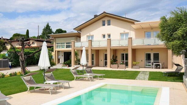 A two-story building with a swimming pool, lounge chairs, and umbrellas.