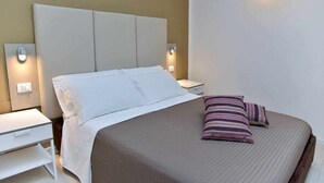 A neatly made bed with a headboard, two bedside tables, and a wall-mounted light fixture.