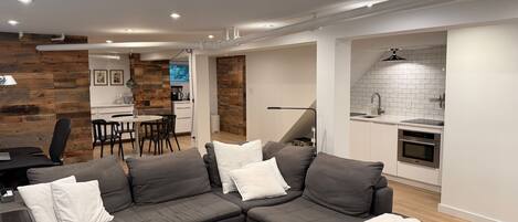 A modern living room with a sectional sofa, a dining area, and a kitchen with white subway tiles.