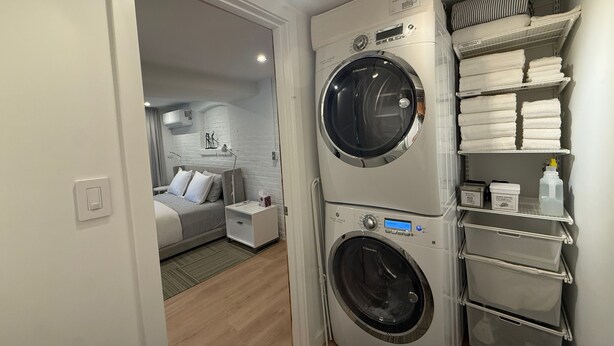 Habitación de hotel pequeña con lavadora, cama, mesita de noche y estante con toallas.