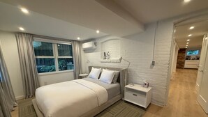 Un dormitorio moderno con una cama grande, mesitas de noche, una ventana con cortinas, aire acondicionado y vistas al exterior.