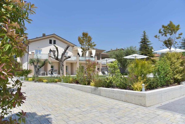 A hotel with a paved courtyard, outdoor seating, and a variety of trees and shrubs.