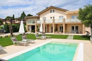 A two-story building with a swimming pool, sun loungers, and a covered patio area.