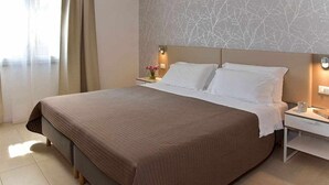 Quarto de hotel com uma cama grande, uma mesa de cabeceira com abajur e uma parede com padrão de árvore.