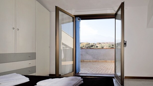 A hotel room with a bed, a wardrobe, and a sliding glass door leading to a balcony with a view of the landscape. - Nice apartment for 6 guests with WIFI, A/C, TV, terrace and pets allowed (Santa Venerina)