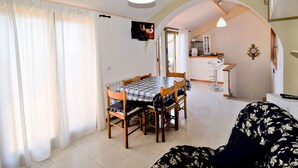 A dining area with a checkered table and chairs, a TV mounted on the wall, and a kitchen visible through an archway. - Nice apartment for 6 guests with WIFI, A/C, TV, terrace and pets allowed (Santa Venerina)