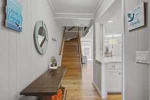 Un escalier en bois menant à un deuxième étage, un coin repas avec une table en bois et une cuisine avec des placards blancs.