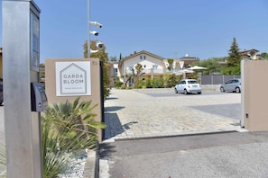 Une entrée fermée par un portail donnant accès à un quartier résidentiel, avec une enseigne indiquant « Garda Bloom Holiday Apartments ».