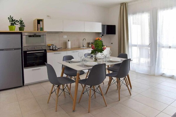 A modern kitchen with a dining area, including a refrigerator, oven, and dining table set with chairs.
