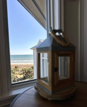 A window view of a beach with a wooden lantern on the windowsill.