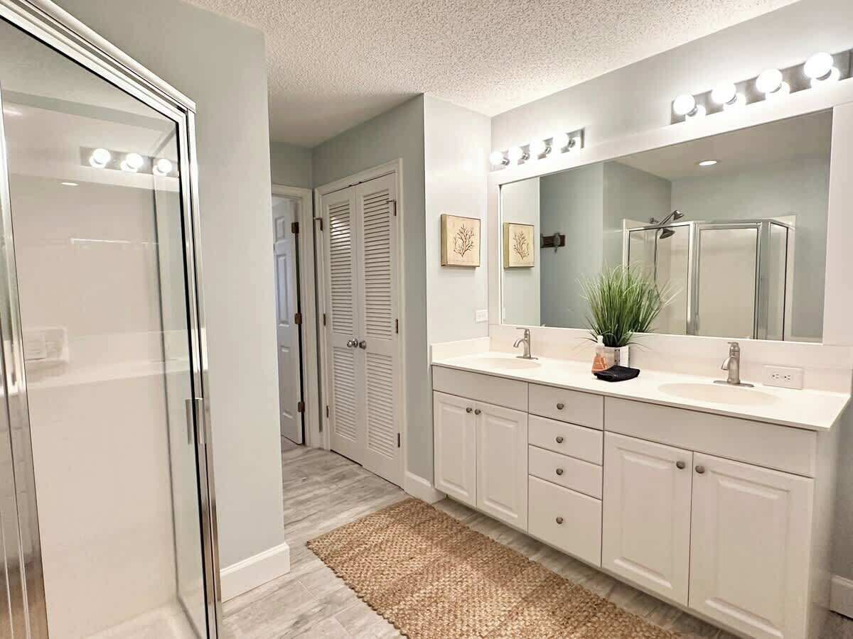 A modern bathroom with a large mirror, two sinks, and a walk-in shower.