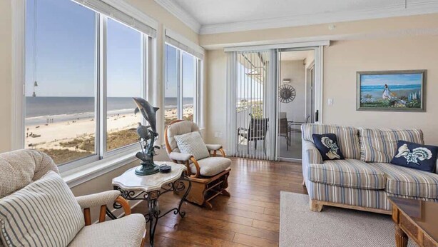 A room with large windows, a striped sofa, a chair, and a table. - Oceanfront Penthouse Villa w/ Balcony, Hilton Head (Hilton Head Island)