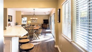 A modern kitchen with a marble countertop, wooden stools, a dining table, and a chandelier.