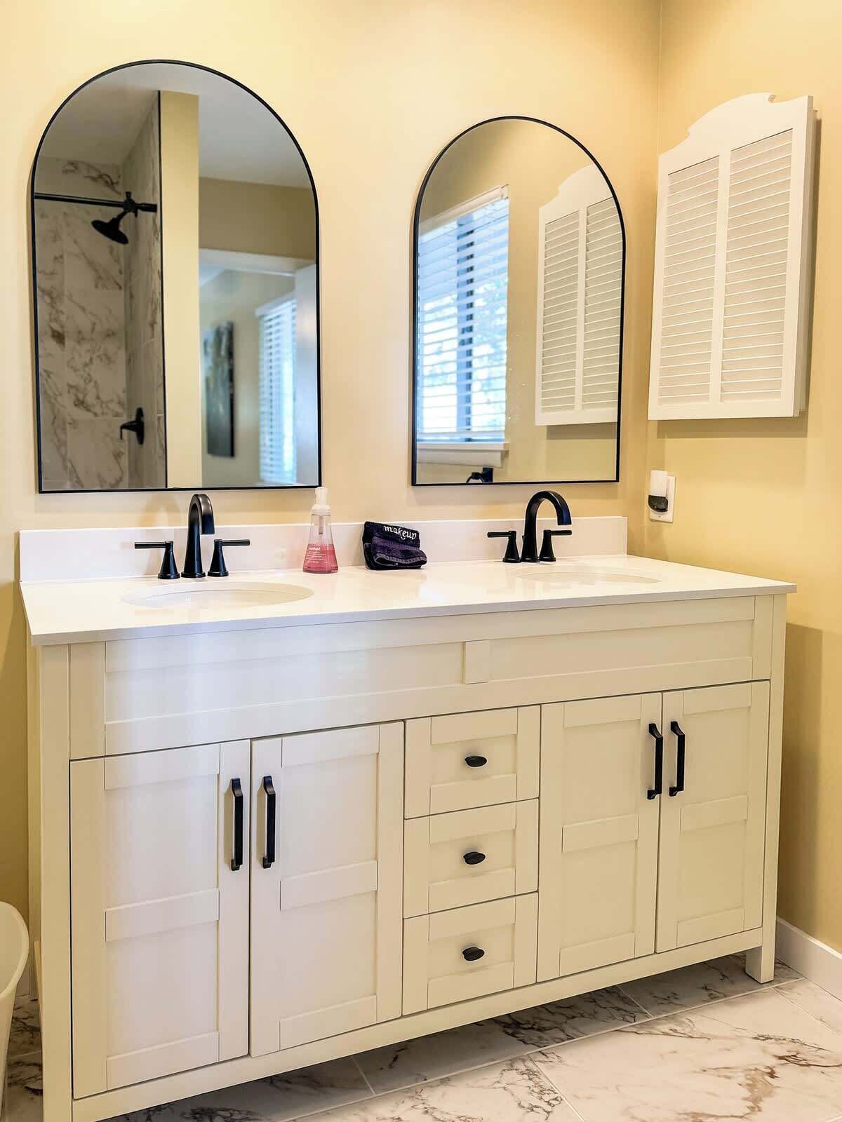 Une salle de bain avec un meuble-lavabo blanc, deux miroirs, un lavabo et une douche.
