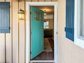 A teal door leading to a room with a window and a light fixture.