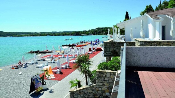 Un hôtel situé en bord de mer, avec un tapis rouge, des parasols blancs et des chaises longues.