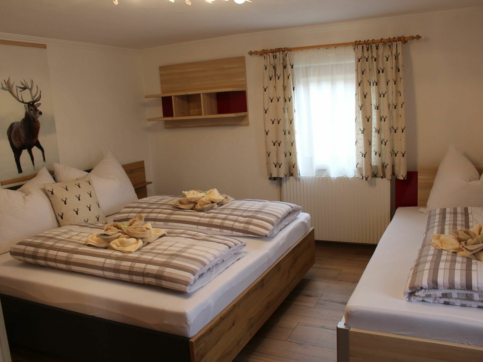 A bedroom with two beds, a wooden headboard, a deer wall art, and curtains with a deer pattern.