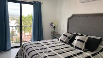 Un dormitorio con cama, una mesita de noche, un jarrón con flores y vistas a través de un balcón.
