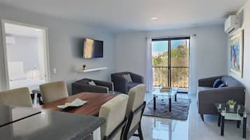 Una sala de estar moderna con comedor, un televisor de pantalla plana en la pared y un amplio ventanal corredizo que da a un patio exterior.