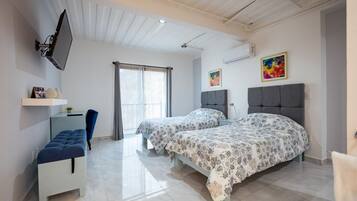 A modern bedroom with two beds, a TV mounted on the wall, a bench, and a window with curtains.