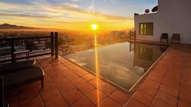 Una piscina infinita con vistas despejadas de la puesta de sol sobre un paisaje urbano.