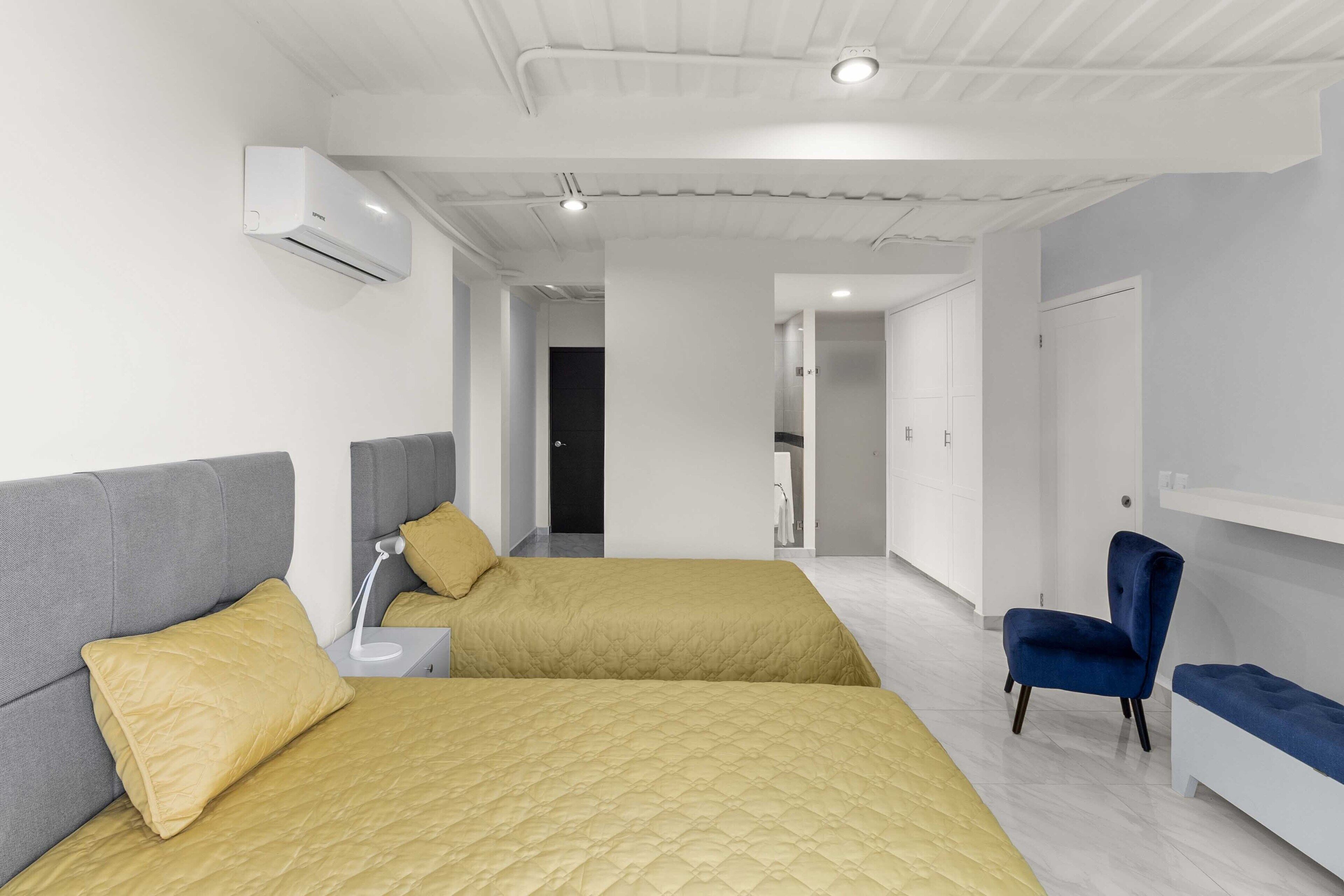 A modern hotel room with two beds, a desk, a chair, and a wardrobe.