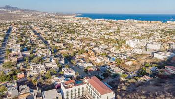 An aerial view of a coastal city with dense residential buildings, a clear blue sea, and a distant mountain range.
