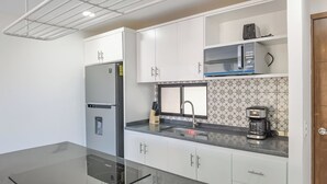 Una cocina compacta con gabinetes blancos, microondas integrado, cafetera y refrigerador.