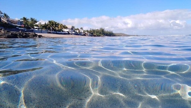 Ein Strand mit klarem, seichten Wasser, das Muster im Sand erkennen lässt.