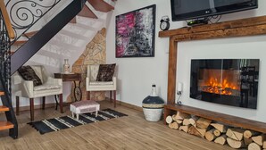 Un salon chaleureux avec une cheminée, un téléviseur fixé au-dessus, un escalier et un tableau au mur.