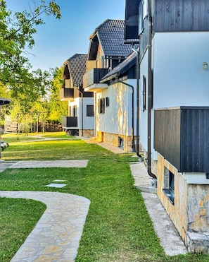 A residential building with a stone pathway, a wooden deck, and a well-maintained lawn.
