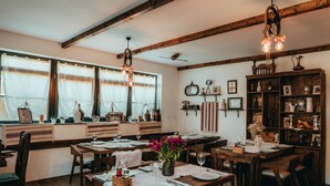 Un espace repas avec des tables et des chaises en bois, un lustre et une bibliothèque remplie de livres et d’objets décoratifs.