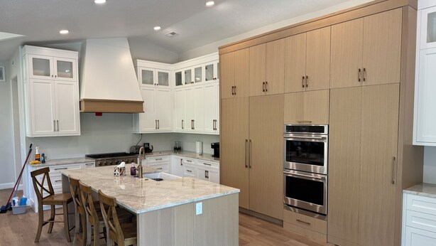 A modern kitchen with white cabinets, a large island with bar stools, and built-in ovens.