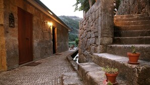 Un edificio de piedra con puerta de madera y un cartel iluminado, un camino empedrado y una escalera de piedra con macetas.