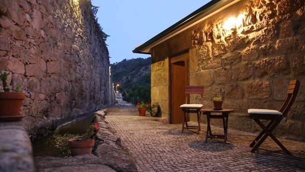 Una calle adoquinada con edificios de piedra, un banco de madera y plantas en macetas.