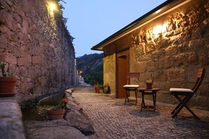 A cobblestone street with stone buildings, a wooden bench, and potted plants.