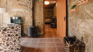 Una habitación rústica con paredes de piedra, techo de madera, una cama con manta escocesa, televisor y chimenea.
