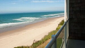 Vista a la playa desde un balcón con barandilla, océano y cielo despejado.