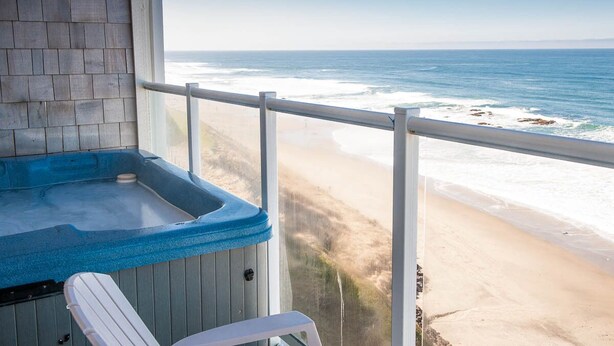 Un balcón con un jacuzzi, una silla y vistas a la playa y al océano.