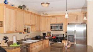 Una cocina con armarios de madera, electrodomésticos de acero inoxidable, encimera de granito e iluminación colgante.